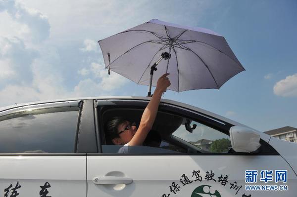 7月20日，在浙江省臨安市一家駕校內(nèi)，一名學(xué)員在車頂架著遮陽傘的教練車內(nèi)練習(xí)。