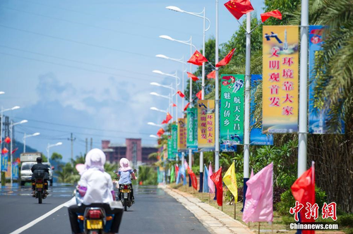 6月24日，海南省文昌市龍樓鎮(zhèn)街道兩側(cè)五星紅旗迎風(fēng)飄揚(yáng)，火箭“首發(fā)”宣傳廣告隨處可見。長征七號運(yùn)載火箭發(fā)射日期臨近，中國首個濱海航天發(fā)射中心——文昌航天發(fā)射場所在地海南省文昌市龍樓鎮(zhèn)將迎來“首發(fā)”，中國的“卡納維拉爾角”正揭開神秘面紗。中新社記者 駱云飛 攝