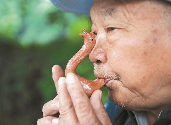 萬富冊老人為過往市民吹奏泥鵝子。